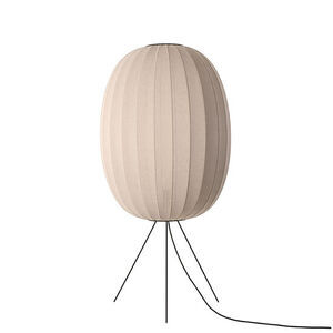 Oval lys beige lampe med strikket overflade på tre sorte ben og en hængende ledning.